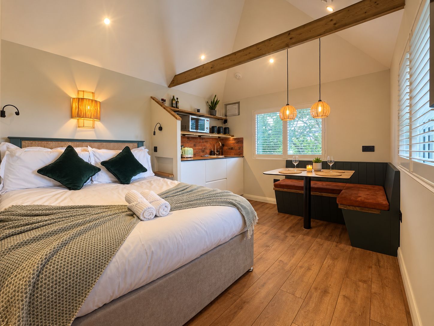 Une chambre avec un lit, des lampes de chevet, un petit coin cuisine et un espace salon avec vue sur l’extérieur.