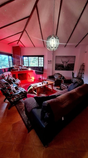 A cozy living room with a large sofa, a coffee table, and a television. There is a window with a view of trees and a painting of a bull on the wall. - La Quinta Esperanza | Country house with a pool, sauna, and natural surroundings (La María)