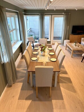 A dining area with a wooden table set for six, surrounded by six chairs, with a television and a sofa in the background. - Inviting, central apartment - Polaris (Tromsø)