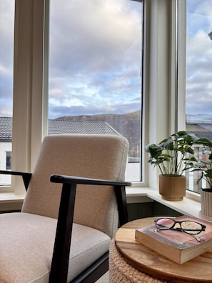 A room with a view of a cloudy sky, a chair, a small round table with a book and glasses, and a potted plant on a windowsill. - Inviting, central apartment - Polaris (Tromsø)