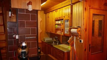 A wooden interior with a kitchen area featuring a brick wall, wooden cabinets, a sink, and a coffee machine.