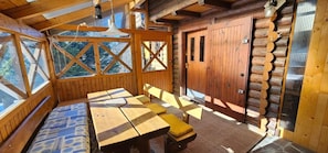 Interior de una cabaña de troncos con comedor, ventanas amplias y una puerta de madera.