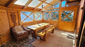 A wooden cabin interior with a stone floor, a table, benches, and a fireplace.