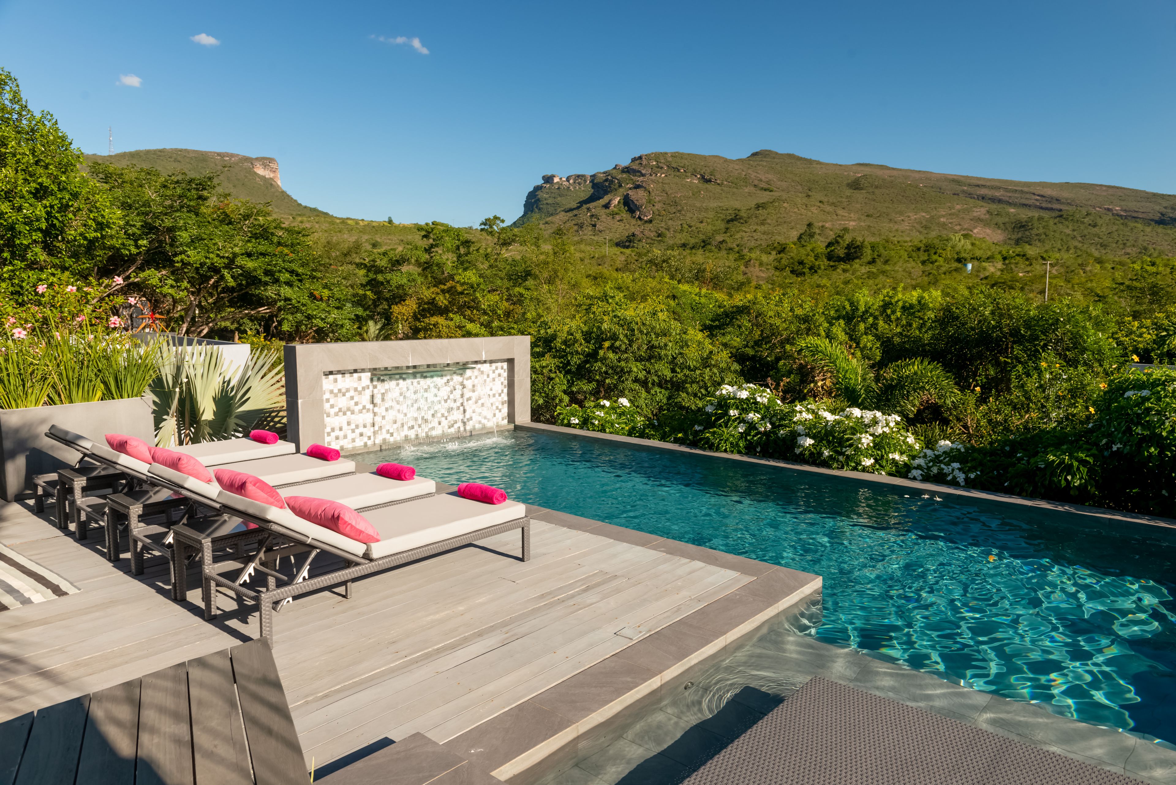 Une piscine à débordement avec une terrasse en bois, des chaises longues et une cascade décorative.