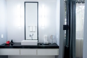 Un baño moderno con un espejo grande, un lavabo blanco y una encimera negra.