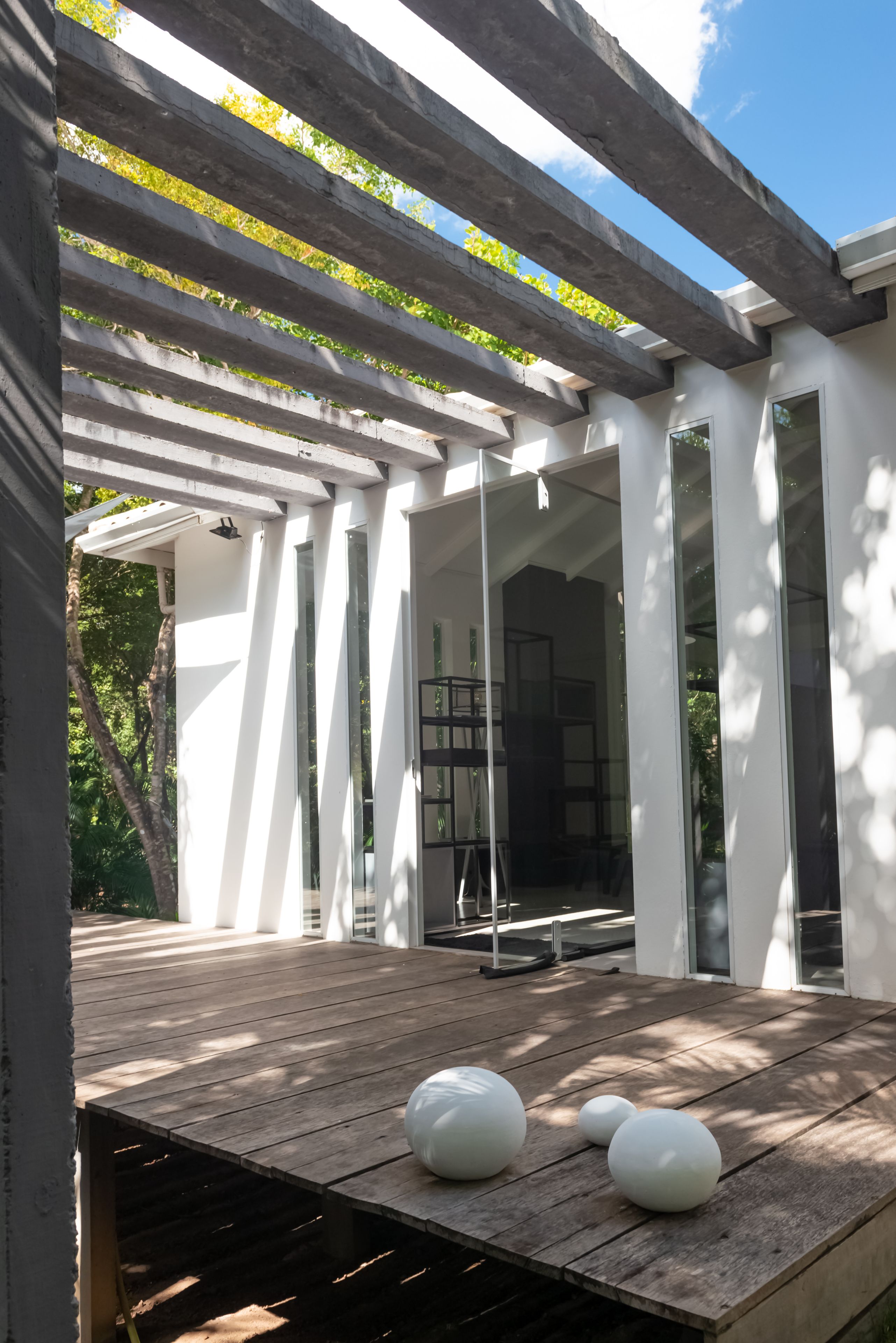 A covered outdoor area with a wooden deck, white columns, and a glass door leading inside.