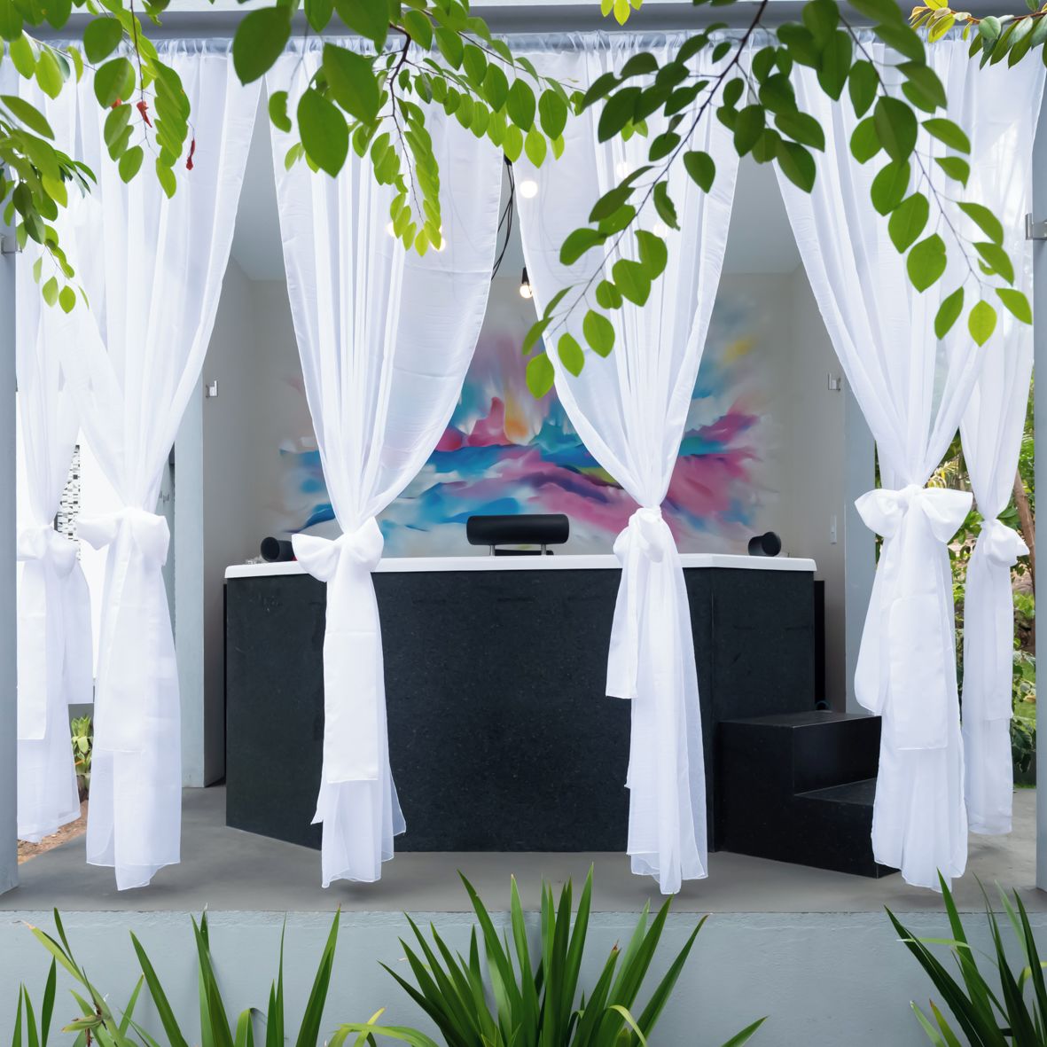 A spa area with a massage table, white curtains, and a colorful abstract painting.