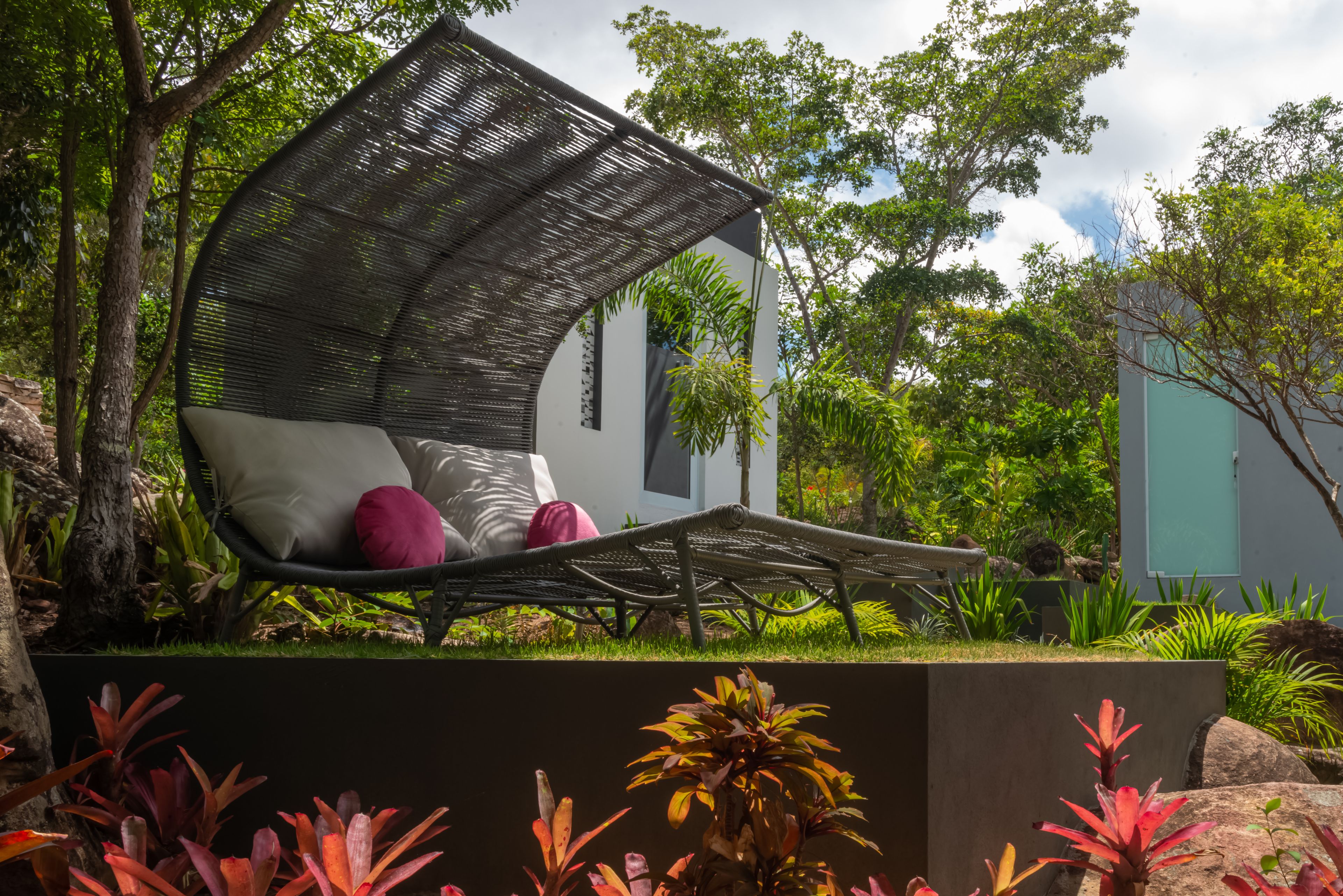 A wicker lounge chair with cushions in a garden setting.