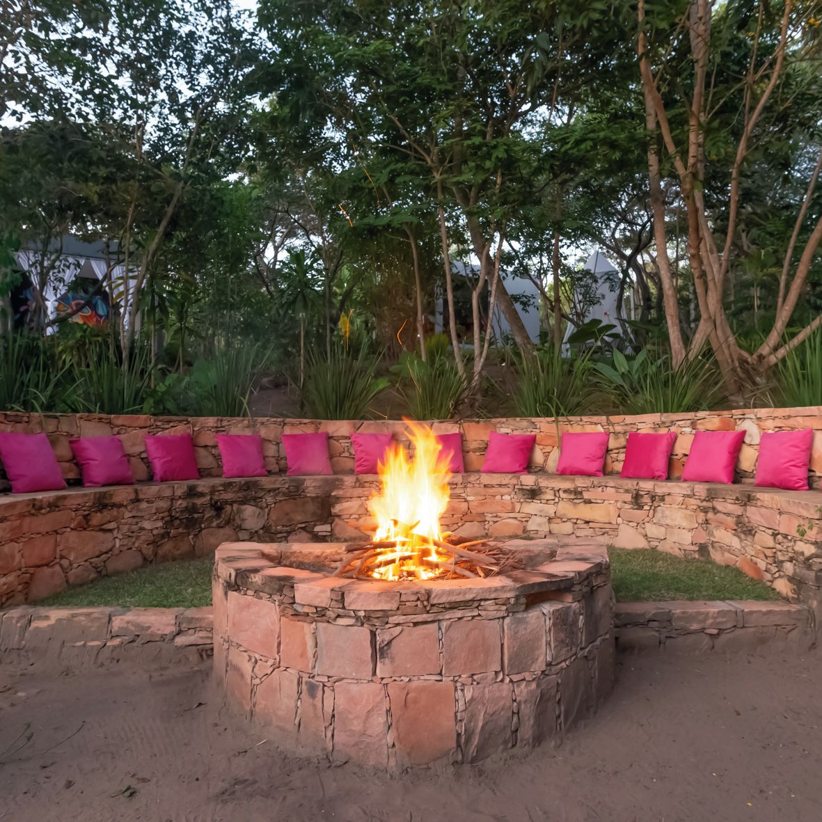 Ein Steinkamin mit Feuer, umgeben von einer Steinsitzbank mit rosa Kissen.