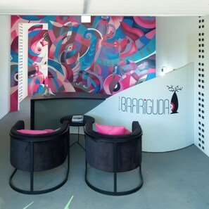 Un interior moderno con un mural abstracto y colorido, una recepción con un logotipo y dos sillas negras acolchadas.
