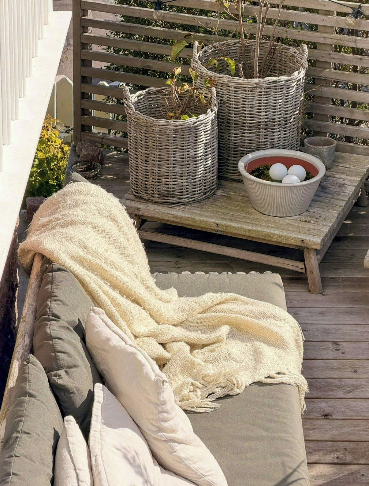 Een houten terras met een rieten mand, een schaal eieren en een bank met kussens.