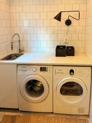 A compact laundry area with a washing machine and dryer, a sink, and a wall-mounted light fixture. - House with jacuzzi and sauna on Smögen (Smögen)