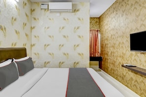 A hotel room with a bed, a TV mounted on the wall, and an air conditioning unit.