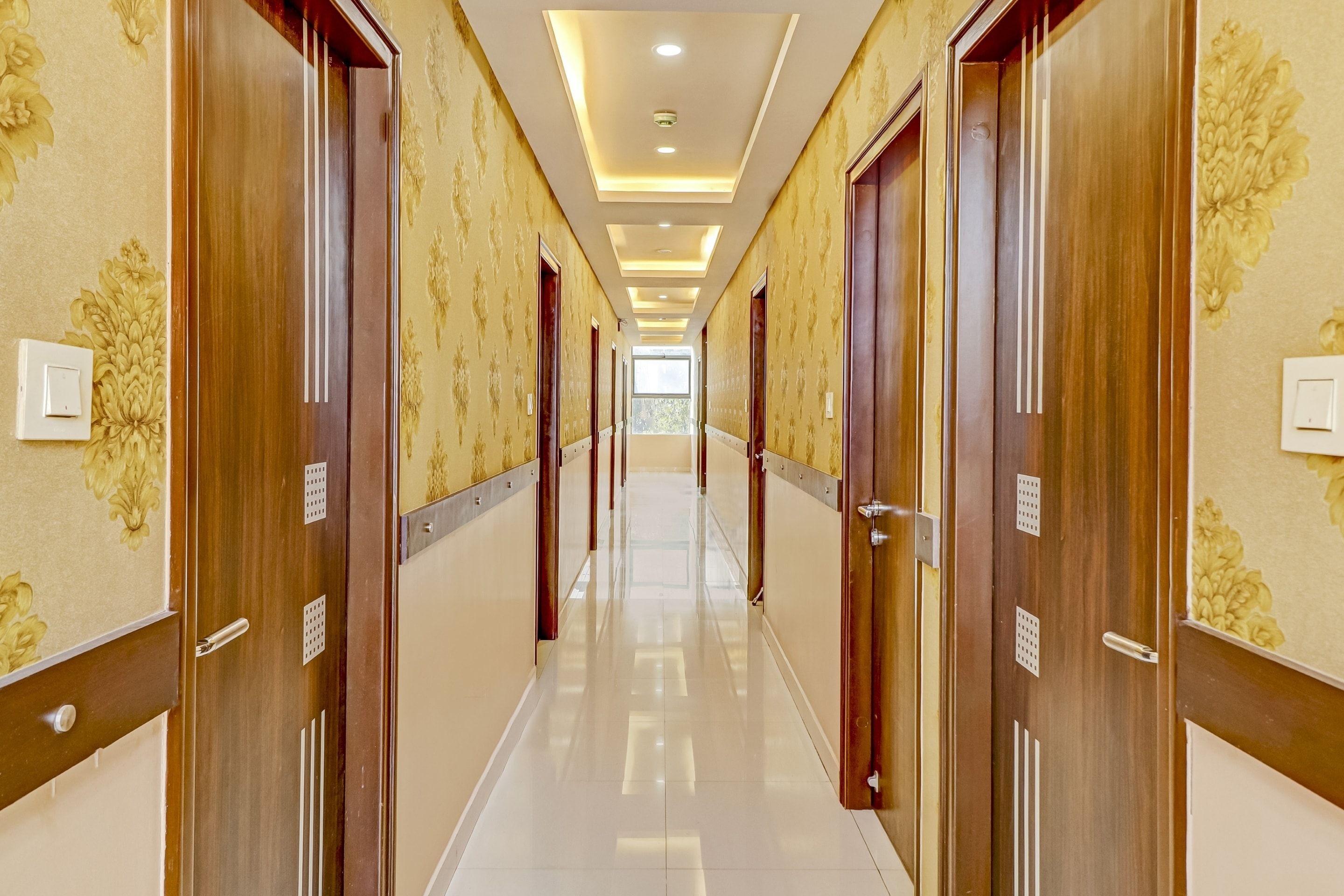 A hotel corridor with wooden doors, patterned wallpaper, and a shiny tiled floor.