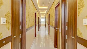 A hotel corridor with wooden doors, patterned wallpaper, and a shiny tiled floor.