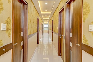 A hotel corridor with wooden doors, patterned wallpaper, and a shiny tiled floor.