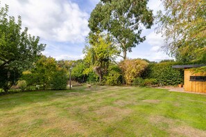 A well-maintained garden with a variety of trees and shrubs, a wooden structure, and a clear sky. - Surrey Hills Family Home With Large Garden (Guildford)