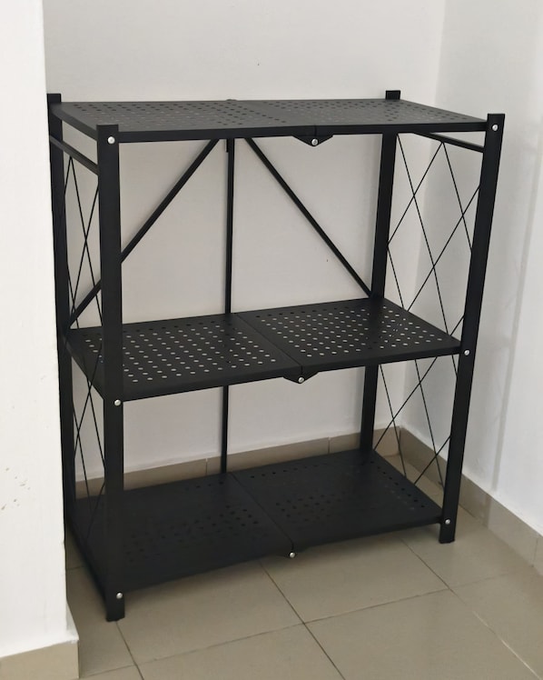 A black metal shelving unit with three shelves, positioned against a white wall. - Palm Court Kuantan (Kuantan)