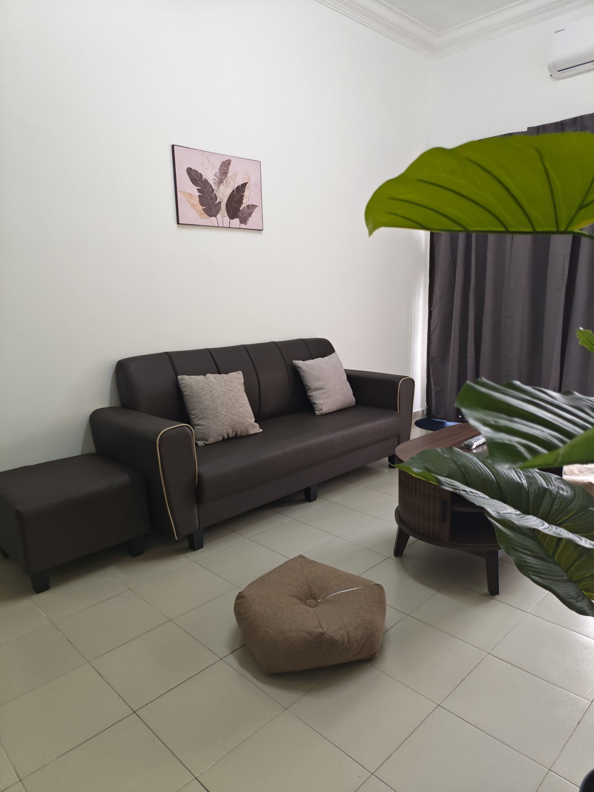 A living room with a sofa, ottoman, and a plant.