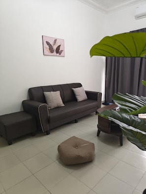 Una sala de estar con sofá, reposapiés y una planta.