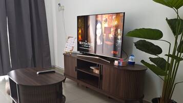 Olohuoneessa on litteänäyttöinen televisio, tumma puinen mediakeskus, pyöreä sohvapöytä, papupussi, ruukussa oleva kasvi ja verho.