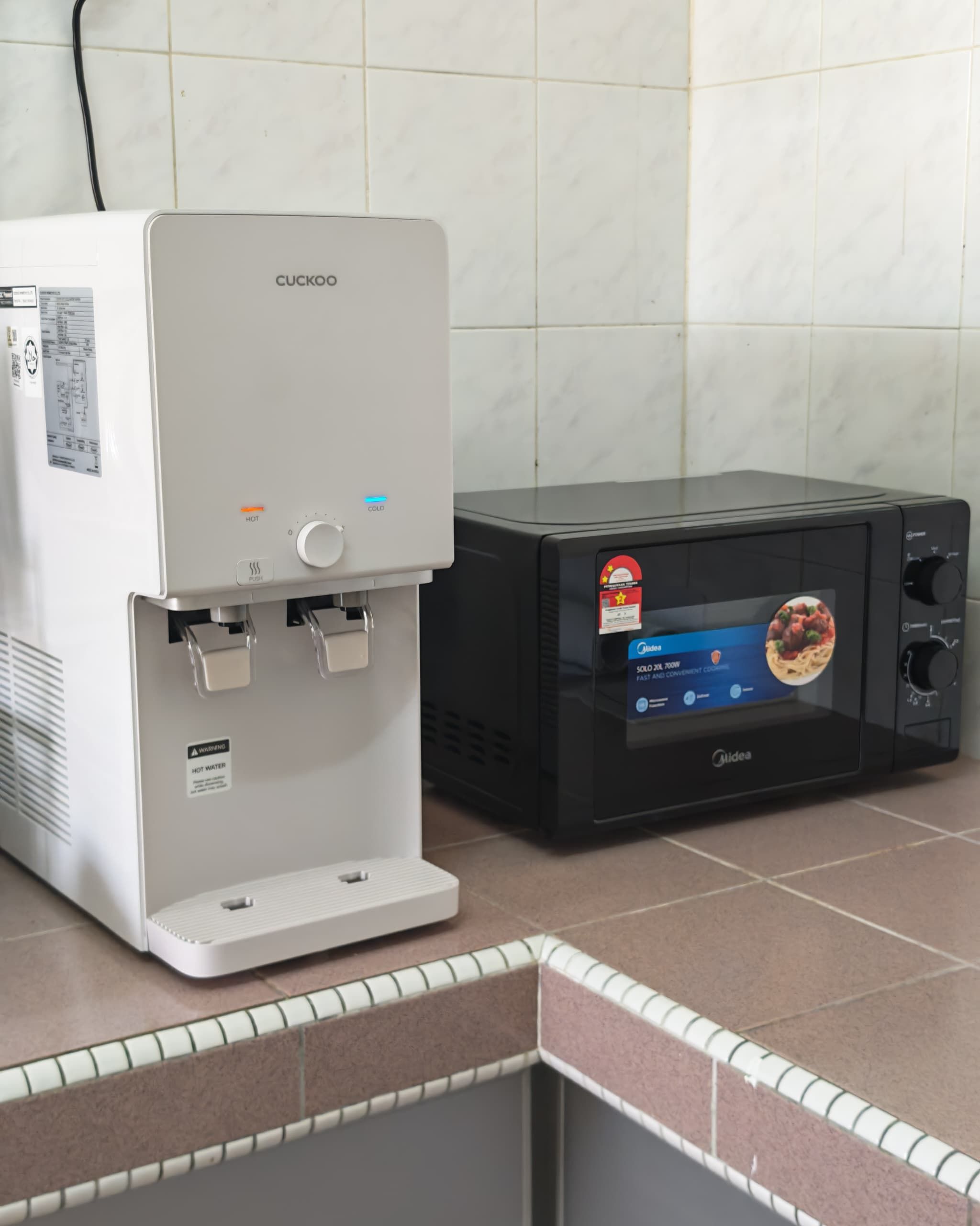 A water dispenser and a microwave on a tiled countertop.