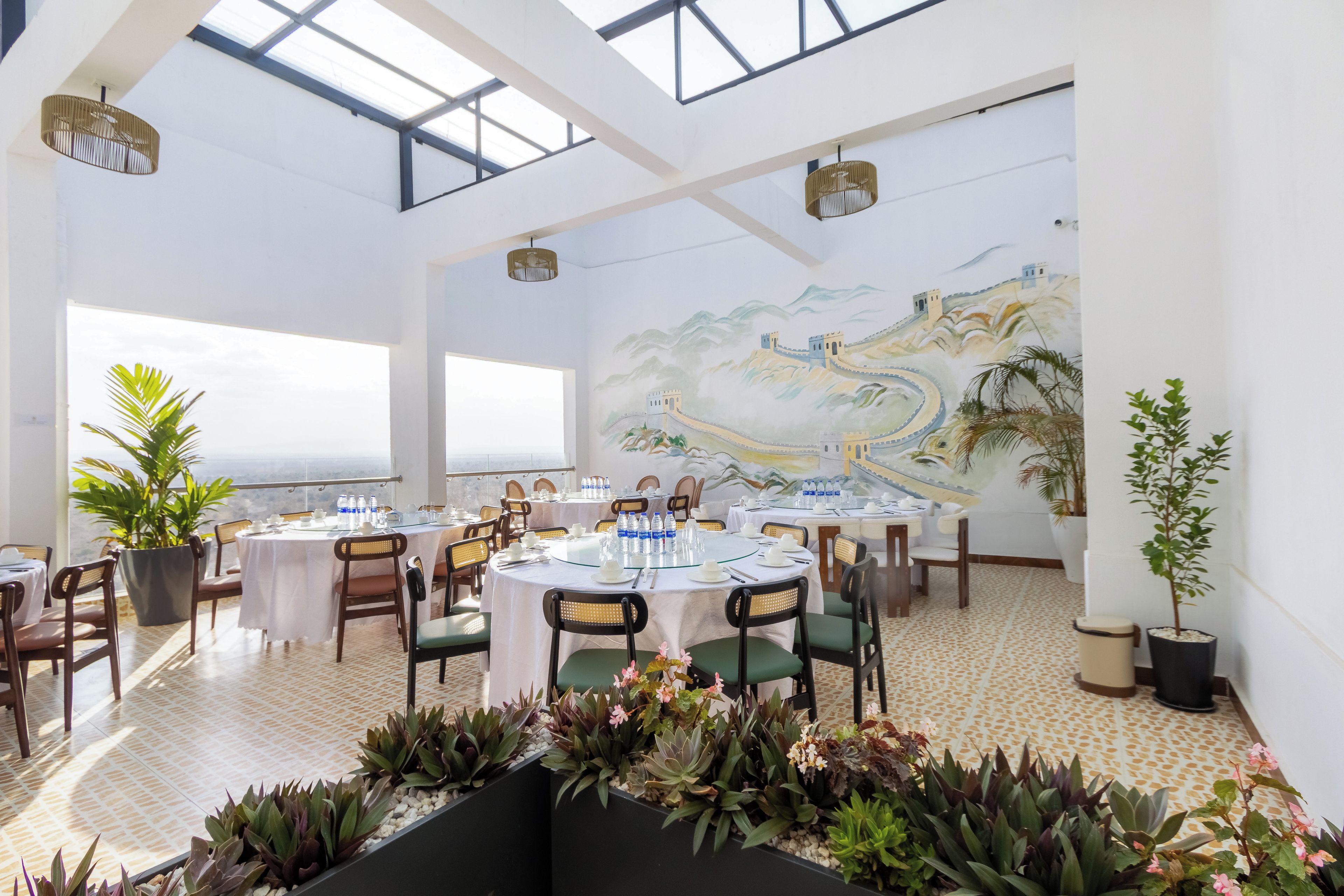 Un restaurante con mesas redondas, sillas y un mural de un paisaje.