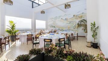 Un restaurante con mesas redondas, sillas y un mural de un paisaje.