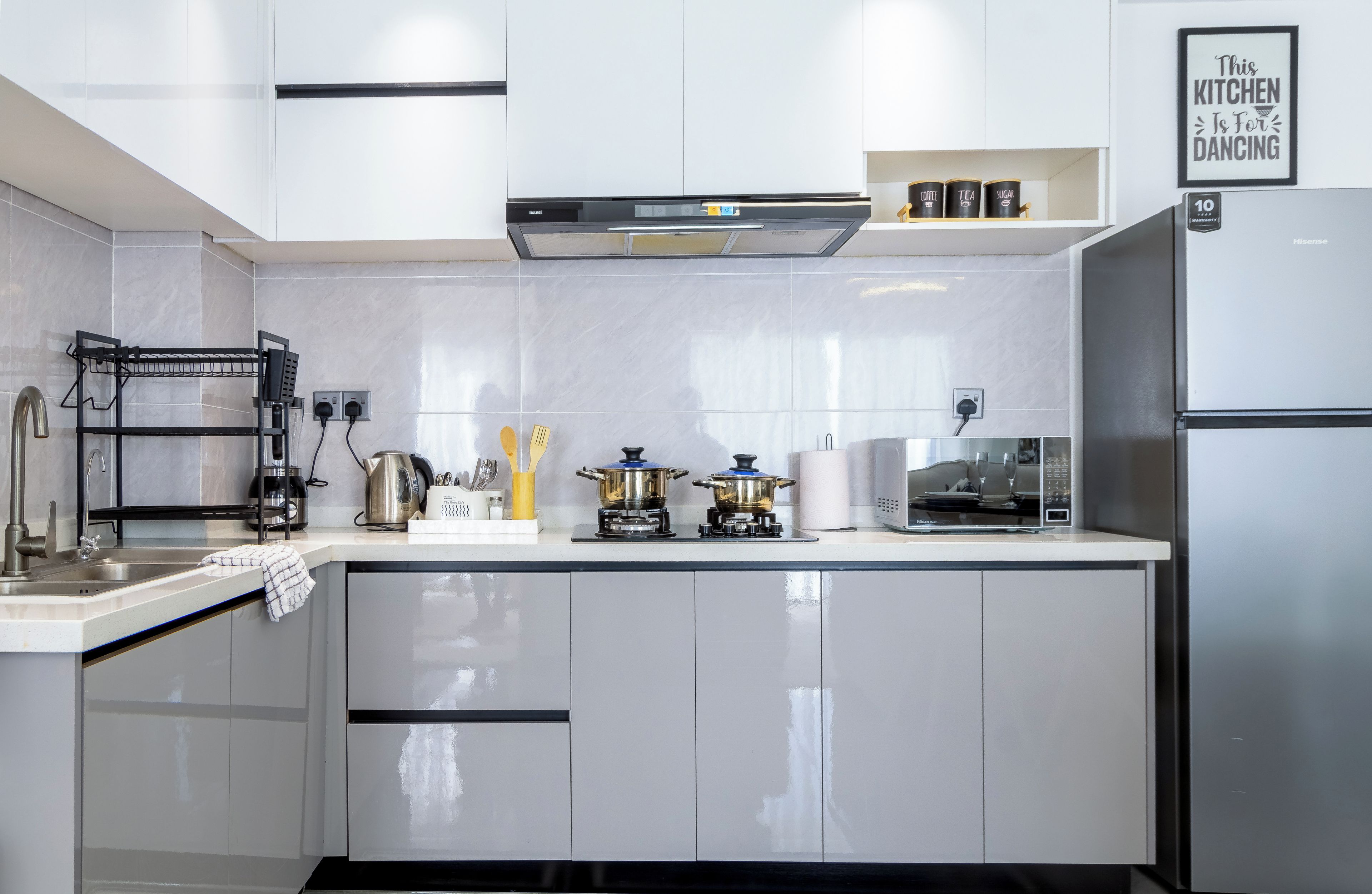 A modern kitchen with white cabinetry, a stainless steel refrigerator, a coffee machine, and a gas stove.