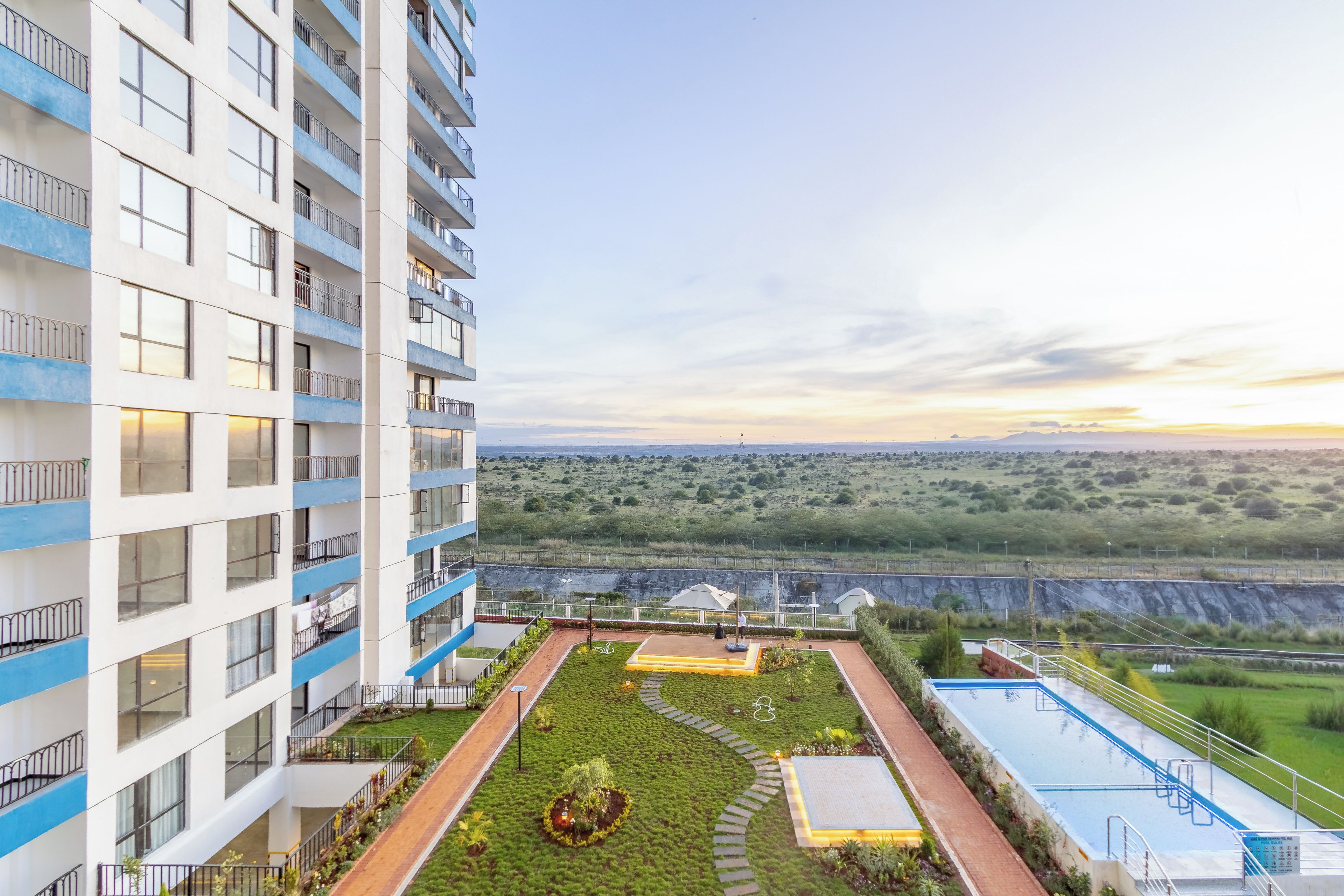 Un edificio alto con numerosi balconi, un'area giardino curata con vialetti e vista su un paesaggio lontano.