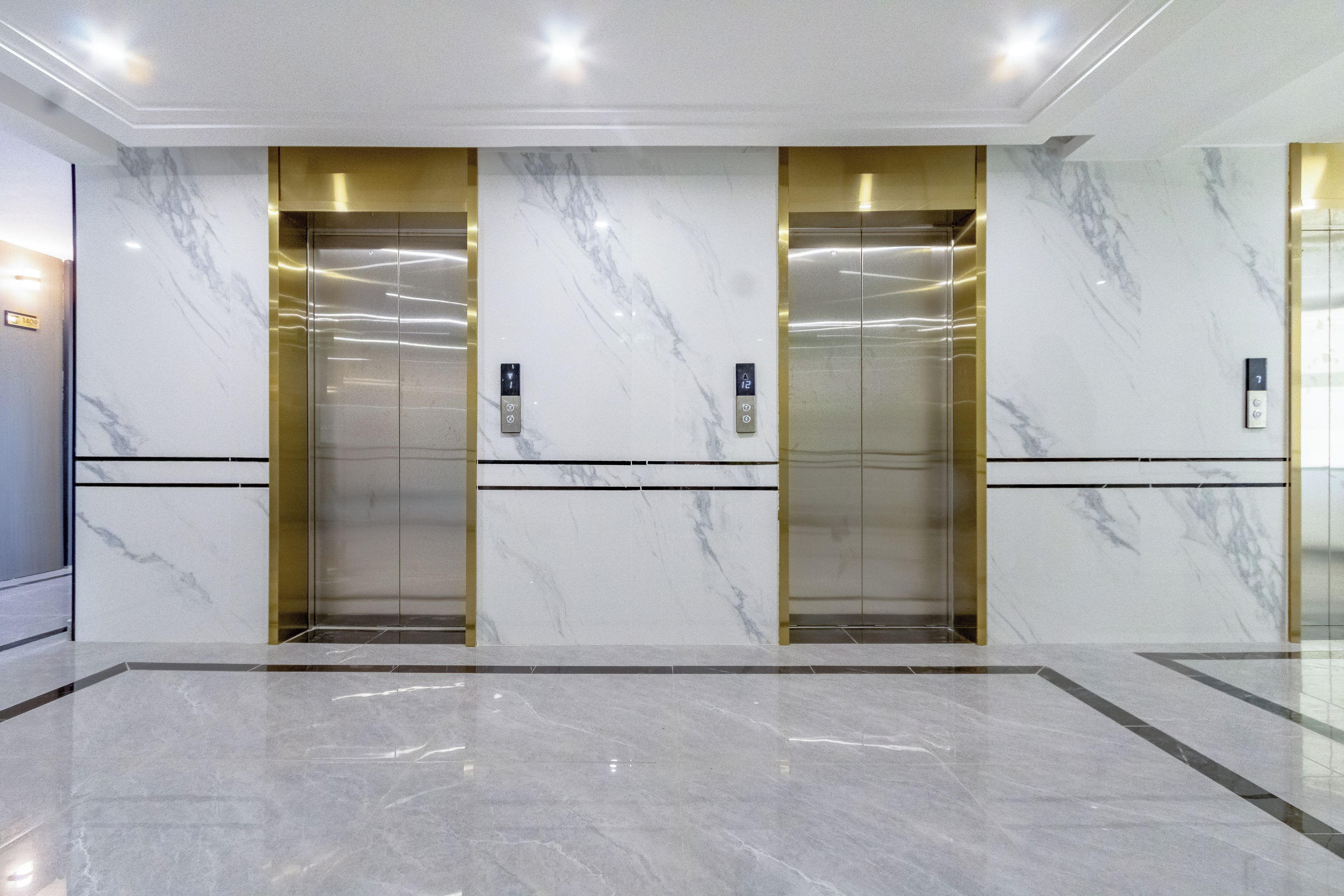 A modern elevator with marble walls and gold accents, located in a well-lit lobby area.