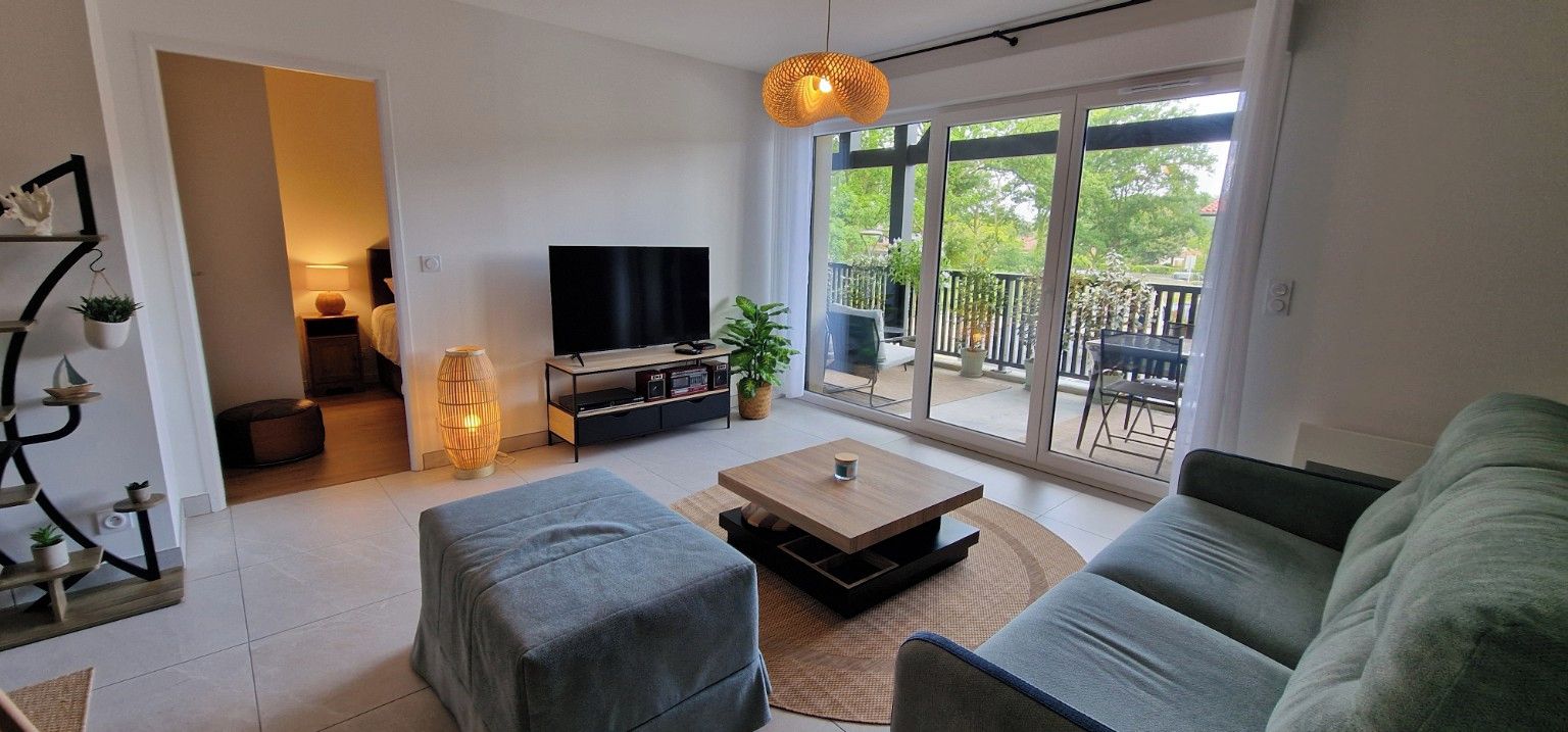 A modern living room with a flat-screen TV, a sofa, a coffee table, and a sliding glass door leading to an outdoor patio.