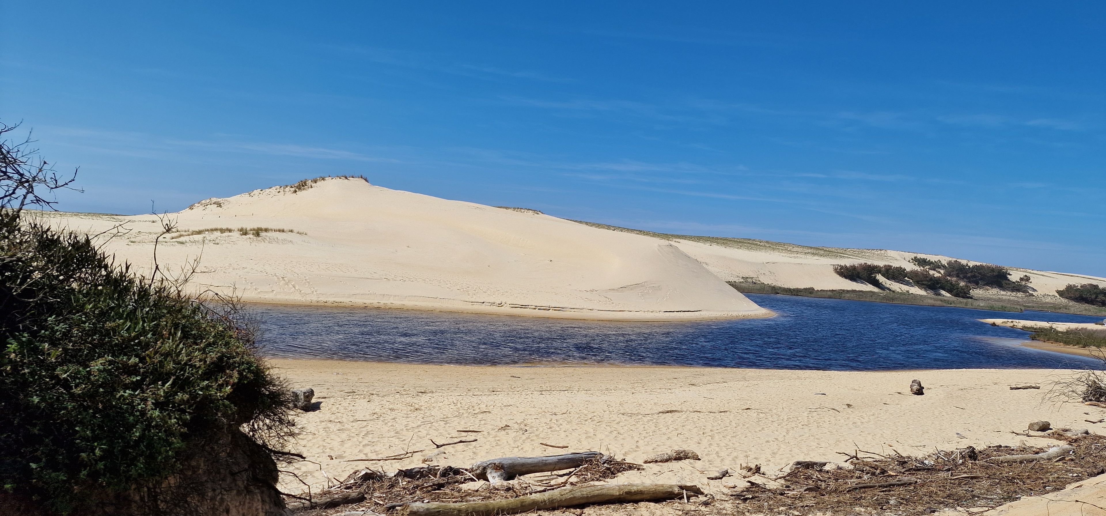Una playa arenosa con una gran duna y una masa de agua tranquila.