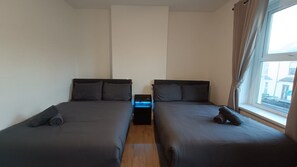Una habitació amb dos llits, una tauleta de nit i una finestra.