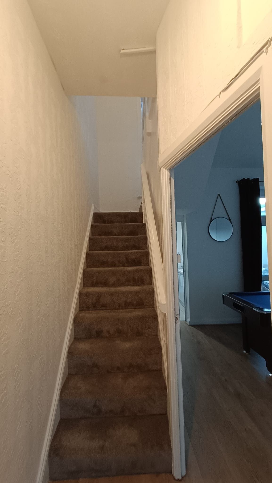 Una escalera alfombrada que conduce a una sala con mesa de billar.