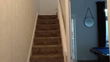 Una escalera alfombrada que conduce a una sala con mesa de billar.