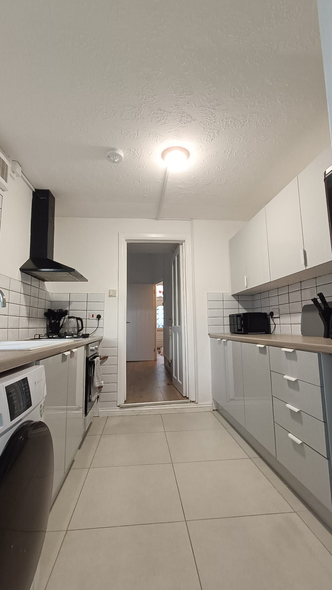 A modern kitchen with white cabinets, a black range hood, a microwave, and a gas stove.