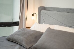 A bed with grey bedding and a headboard, a bedside lamp, and a window with curtains. - Vibrant Japantown Townhome | Walk to Dining (San Jose)