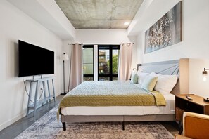 A modern hotel room with a large bed, a flat-screen TV, a desk, and a window with a view of the outdoors. - Vibrant Japantown Townhome | Walk to Dining (San Jose)