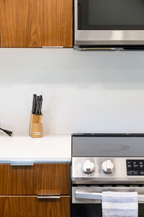 A kitchen with wooden cabinets, a stainless steel microwave, and a stove with a control panel. - Modern J-Town Townhome | Bright & Stylish (San Jose)