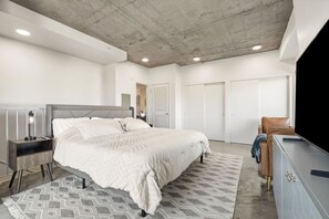 Un dormitorio con cama, mesitas de noche, cómoda, televisor y armario.