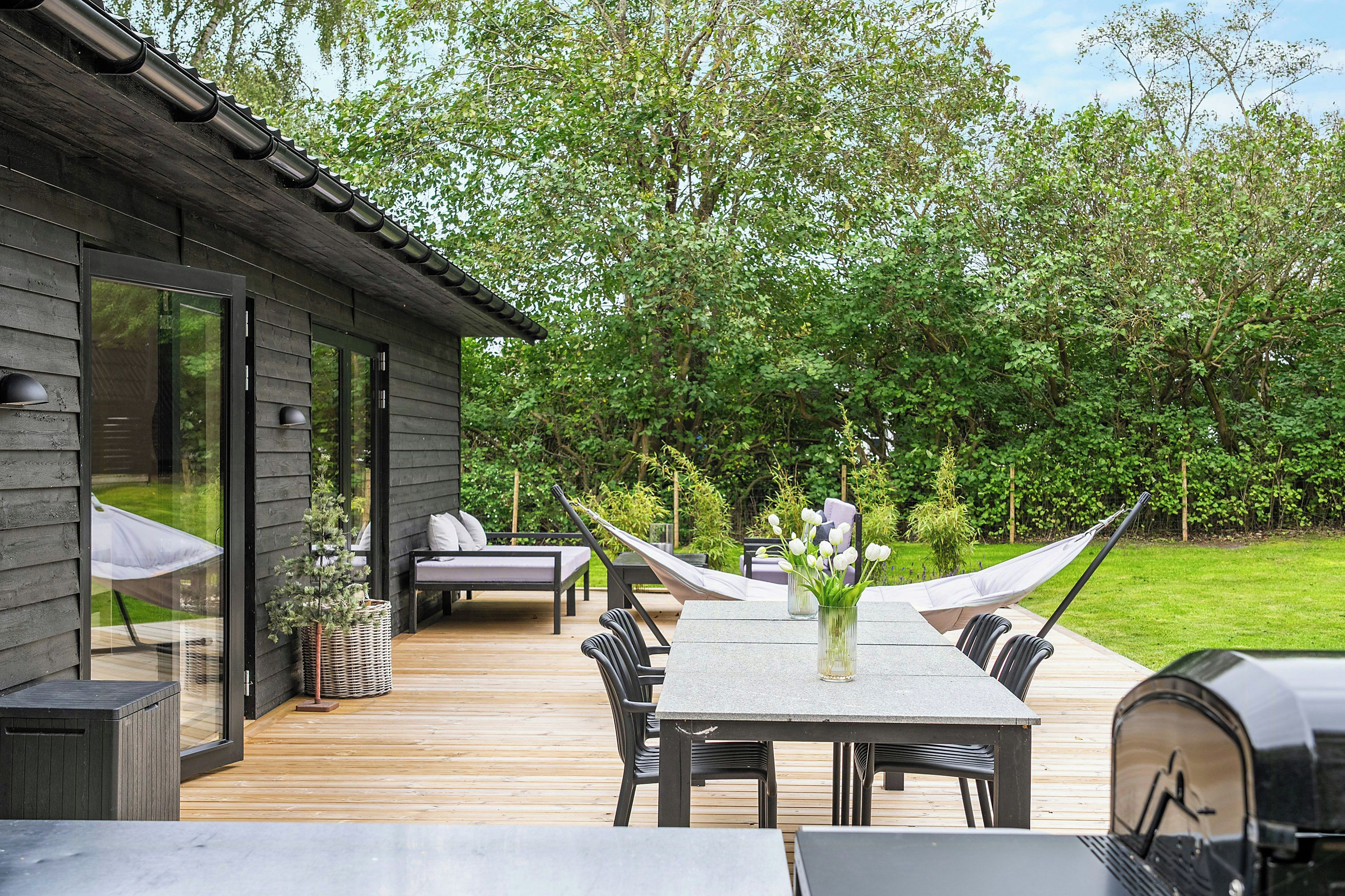 A modern outdoor deck with a dining table, chairs, and a barbecue grill.