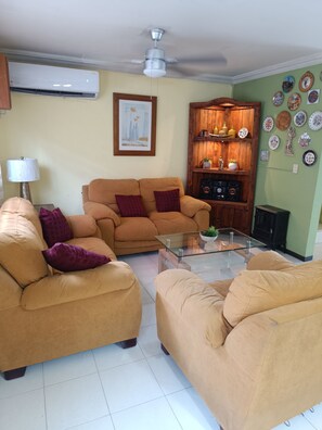 Ein Wohnzimmer mit einer Sofagarnitur, einem Glastisch, einem Deckenventilator und einer Wand mit dekorativen Tellern.
