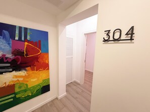 A hallway with a colorful abstract painting on the left and a door with the number '304' on the right. - Modern Downtown Loft Walk2Beach I CasaAmarilla304 (Oranjestad)