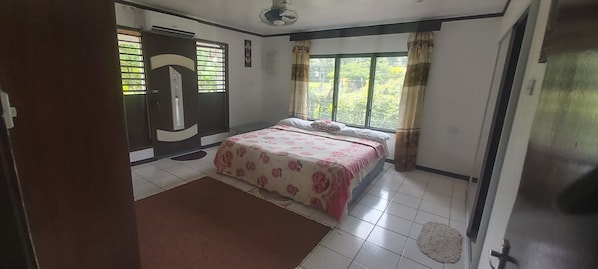 A bedroom with a bed, a window with curtains, a door, and a ceiling fan.