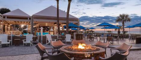 An outdoor seating area with chairs and a fire pit, overlooking a beach.