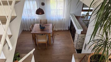 Un comedor con una mesa y sillas de madera, una lámpara colgante y vistas al exterior a través de cortinas translúcidas.