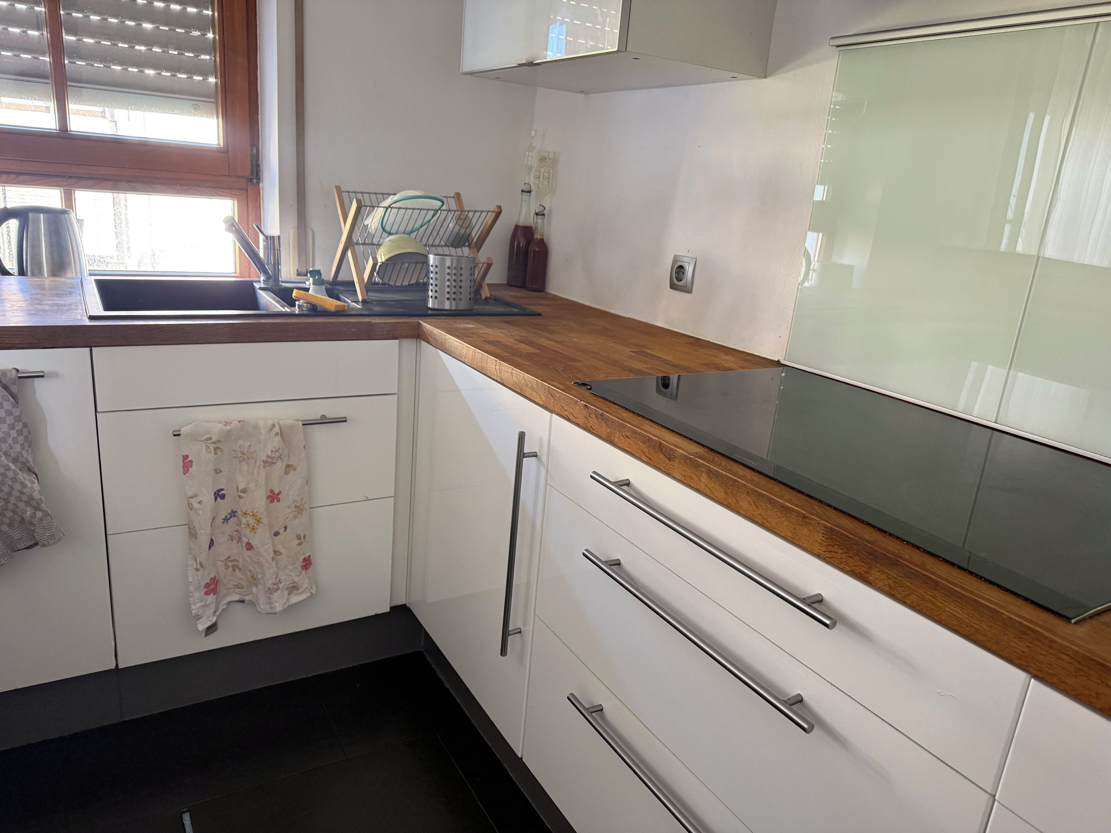 A kitchen with white cabinets, a wooden countertop, a stainless steel sink, and a window with blinds.