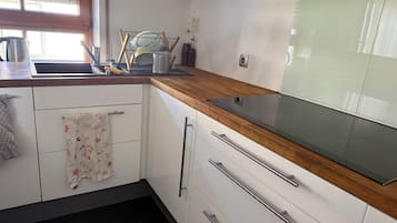 A kitchen with white cabinets, a wooden countertop, a stainless steel sink, and a window with blinds.