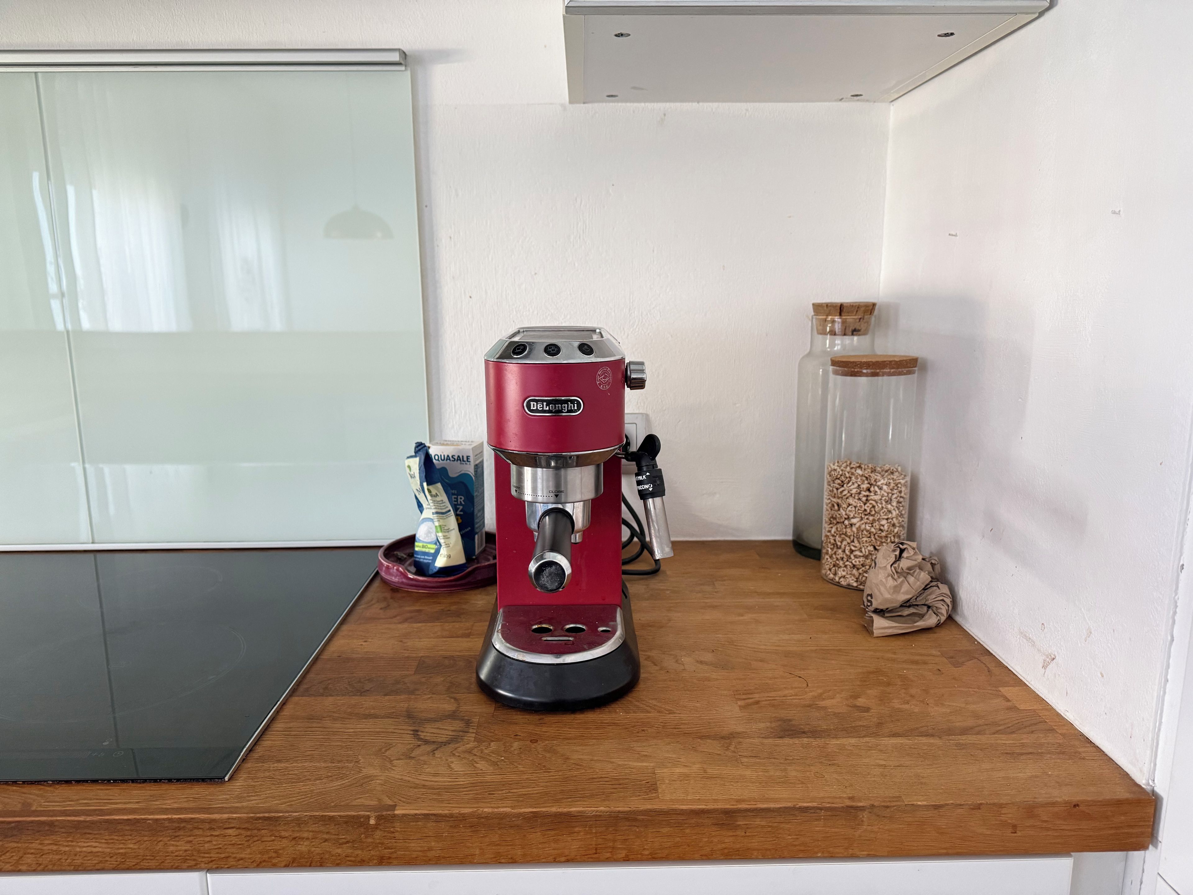 Eine rote Espressomaschine auf einer Holzauskładung, zusammen mit einem Glasbehälter mit Kaffeebohnen und einer Kapselbox.